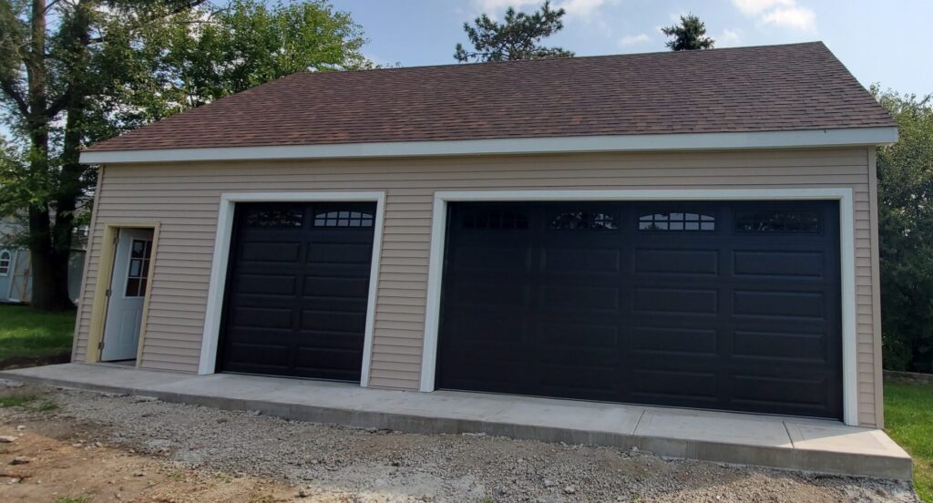 New detached garage construction with vinyl siding, black overhead doors, and concrete apron