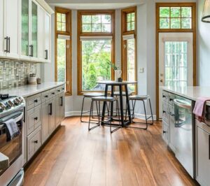Before-and-after kitchen remodel showing updated gray cabinetry, wood flooring, modern finishes, and improved layout