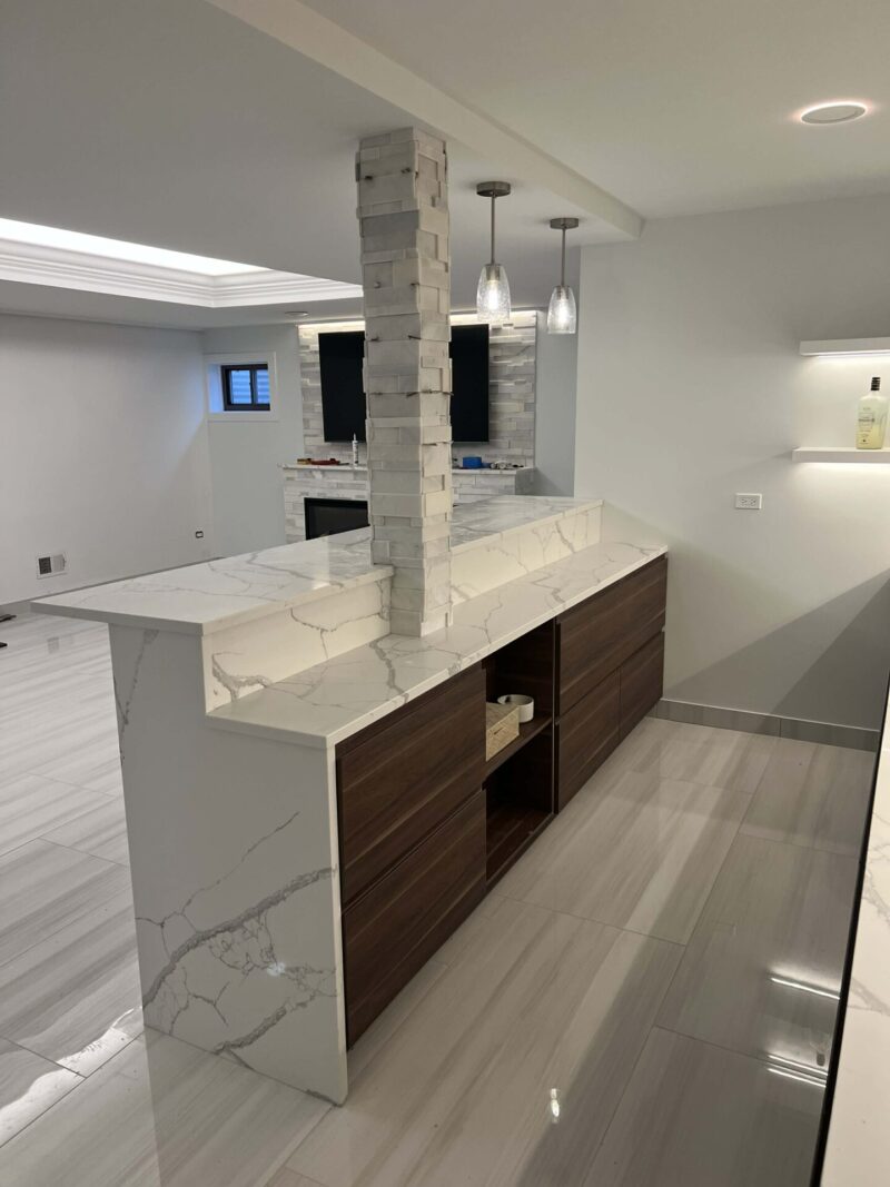 Basement bar with waterfall quartz countertops, wood cabinetry, pendant lighting, and modern tile flooring