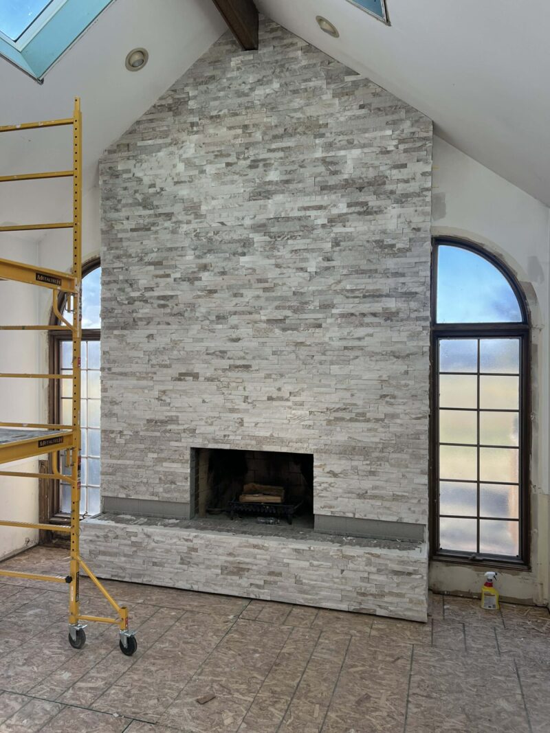 Two-story fireplace wall with full-height stacked stone surround, vaulted ceiling, and arched windows